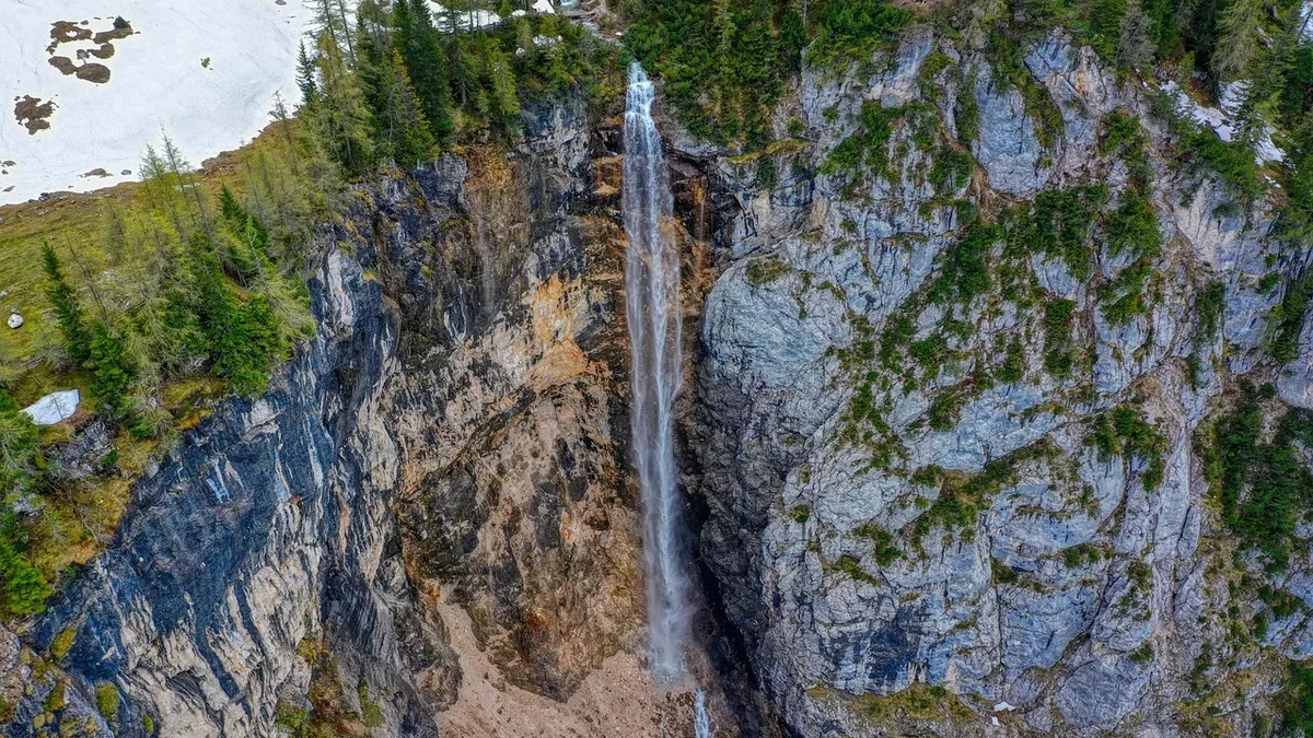A tall waterfall cascading down a rocky cliffside, surrounded by trees and snow.